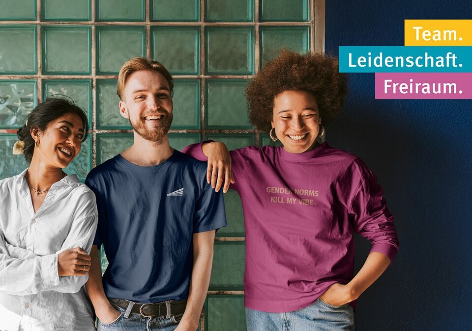 Das Bild wirbt für: "Pädagogische Fachkräfte – Karriere auf der Didacta 2026 Köln" Auf dem Bild stehen drei Personen nebeneinander und lachen gemeinsam. Links trägt eine Frau ein weißes T-Shirt. In der Mitte steht ein junger Mann mit blonden Haaren. Rechts ist eine Frau mit Afrofrisur zu sehen.